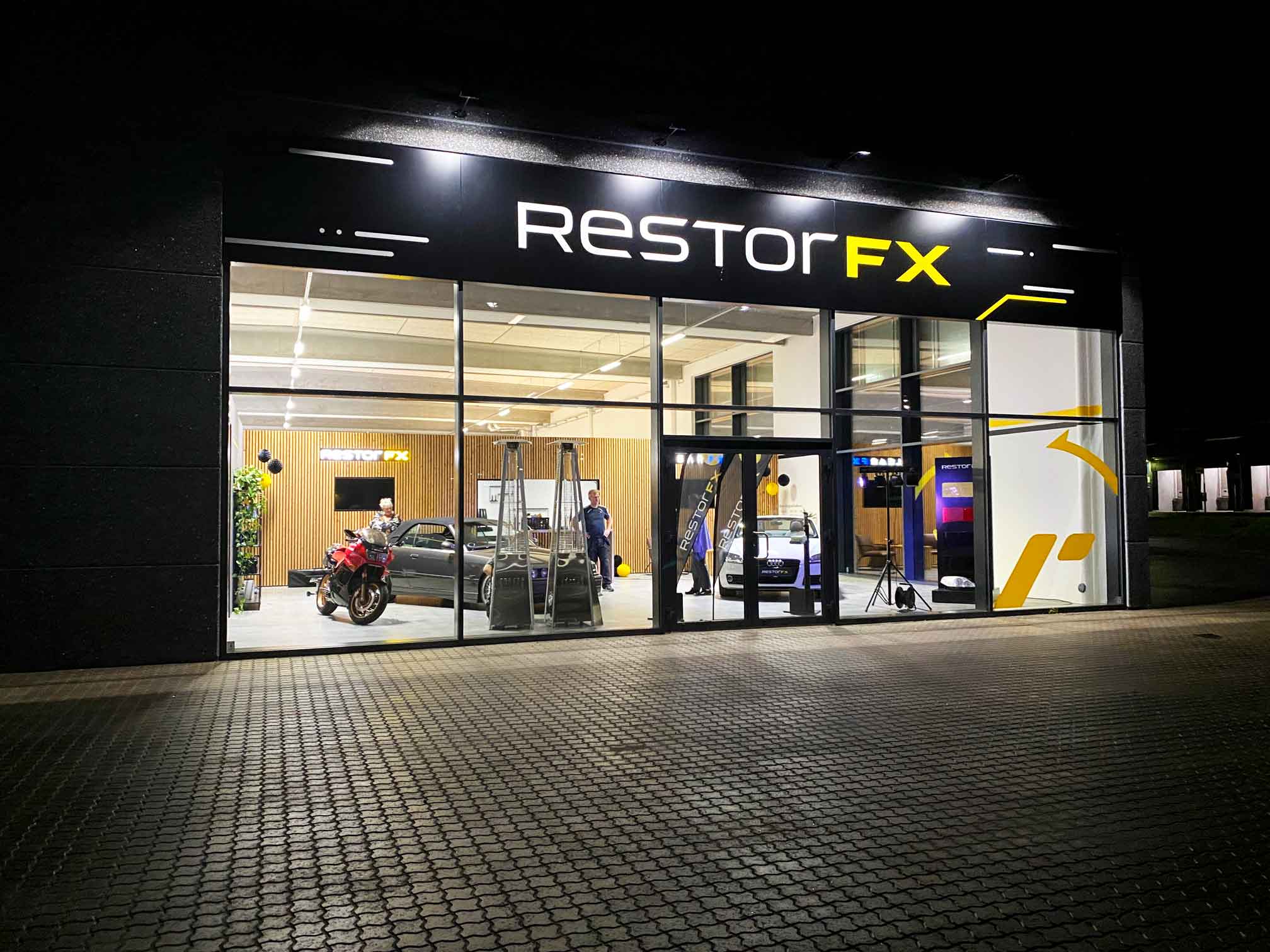 RestorFX Silkeborg storefront with lit branded signage and see-through glass panels during night