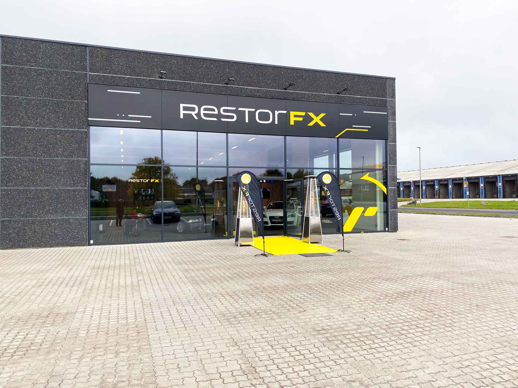 Branded storefront with teardrop flag banners and glass panels during daytime at RestorFX Silkeborg