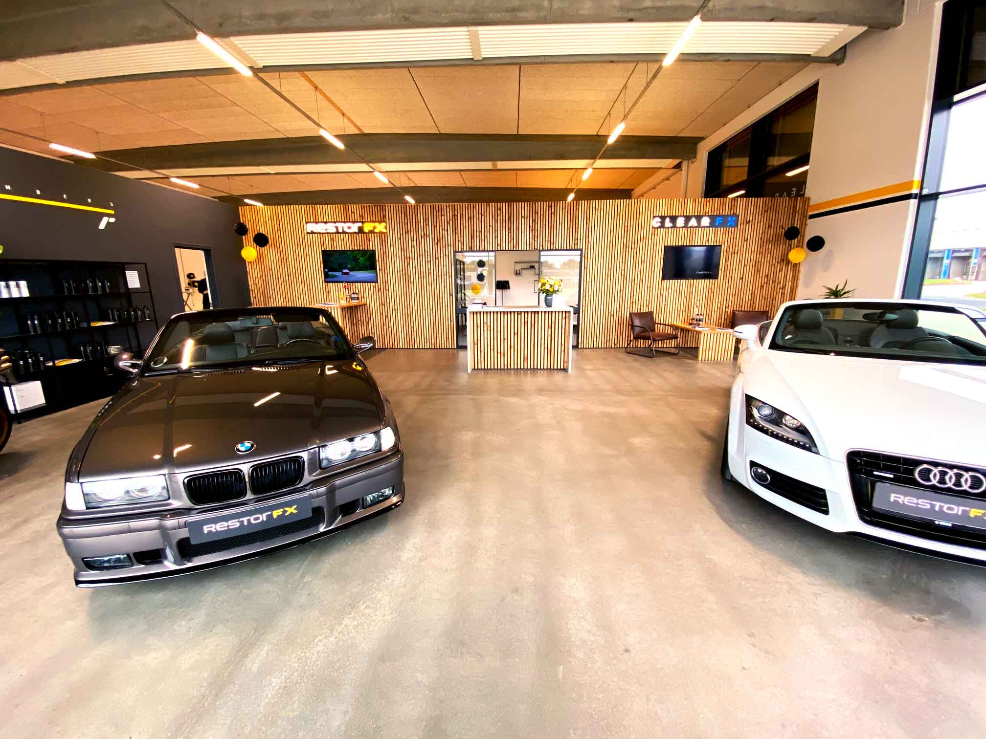Silver BMW and white Audi convertibles inside RestorFX Silkeborg showroom with wooden background