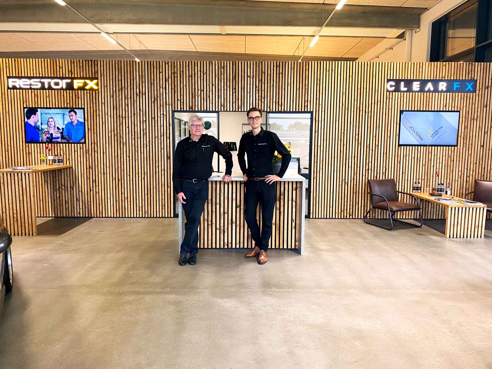RestorFX Silkeborg team posing in front of office area with wooden textured walls and branded decor