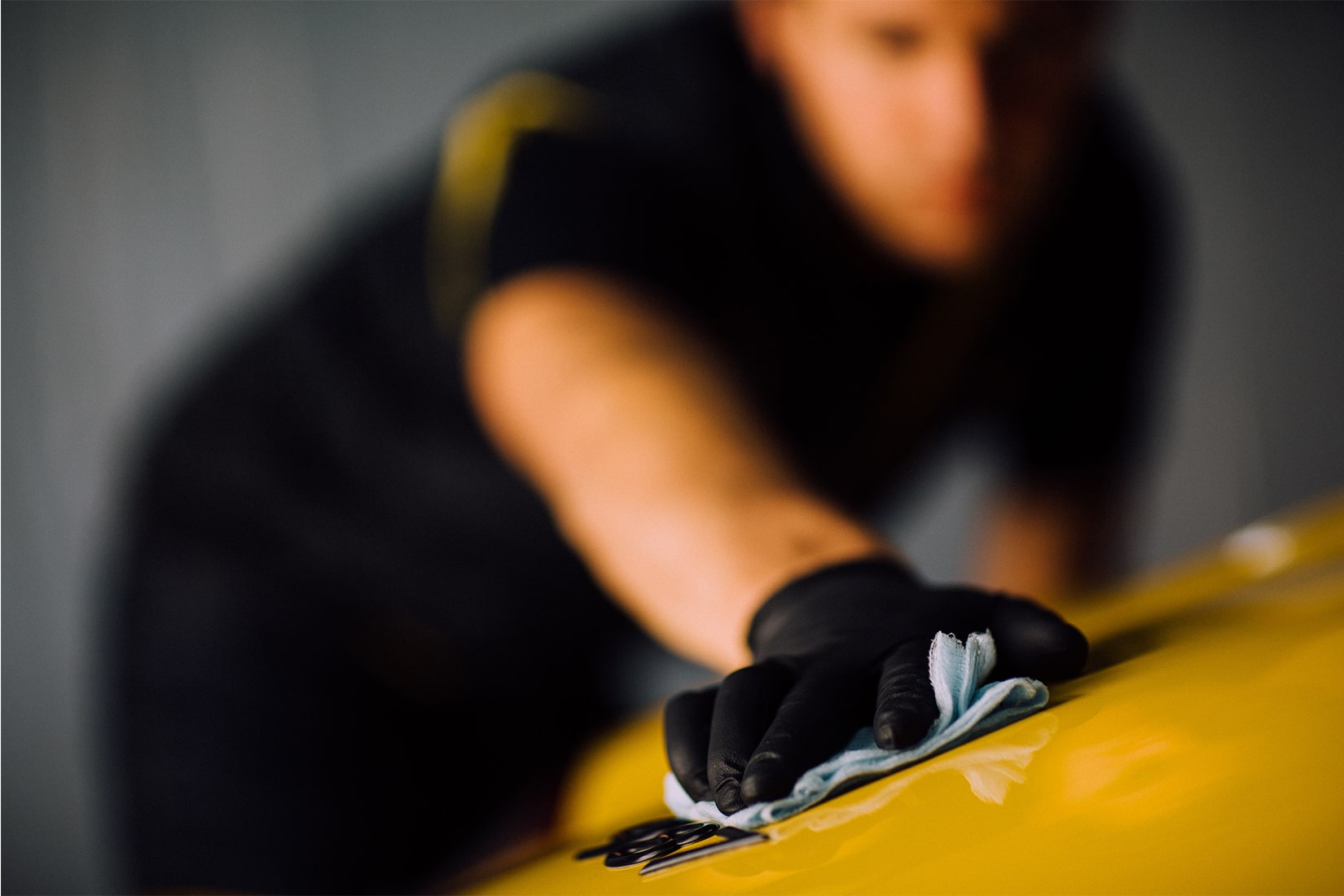 A RestorFX technician cleaning a sleek yellow sports car with a tack cloth in preparation for surface restoration